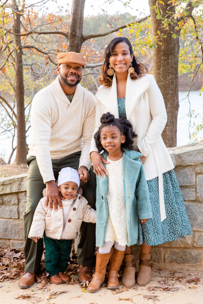 Family photo of four with two toddlers standing in front of a pond in an Atlanta park