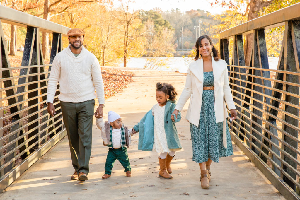 Parents holding toddlers hands and walking on a bridge in Murphey Candler Park Atlanta GA during fall family photo session