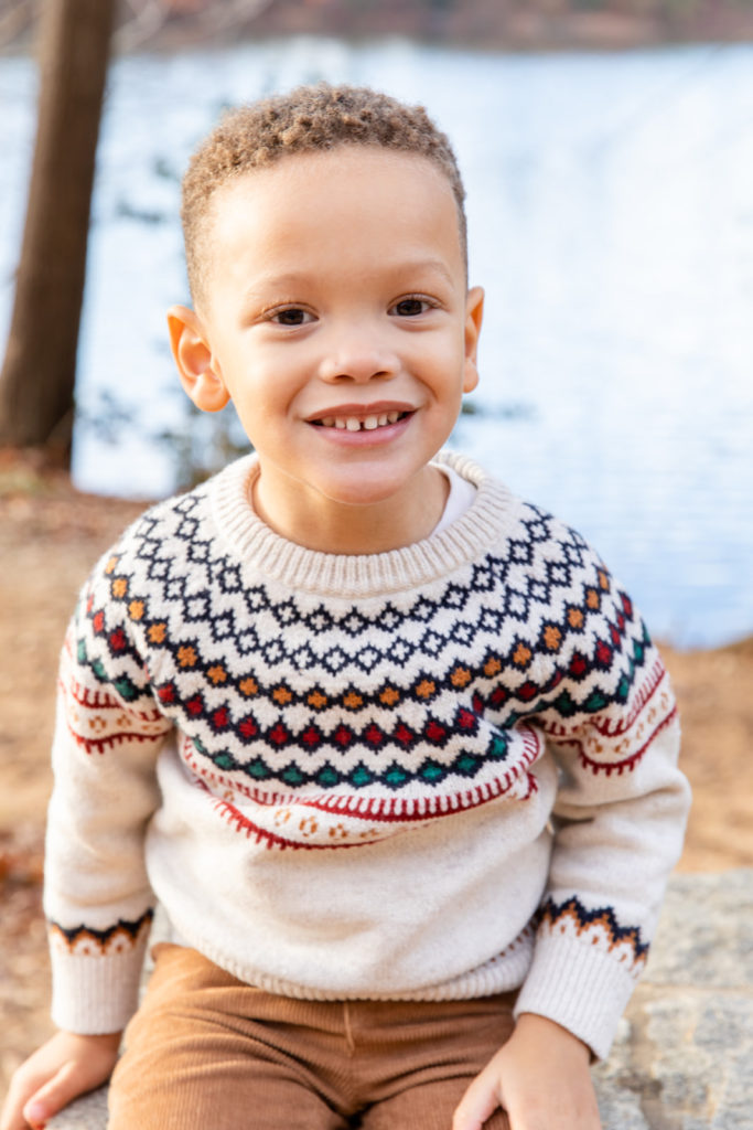 Toddler boy with Christmas sweeter standing in front of a pond during family photo session in Atlanta