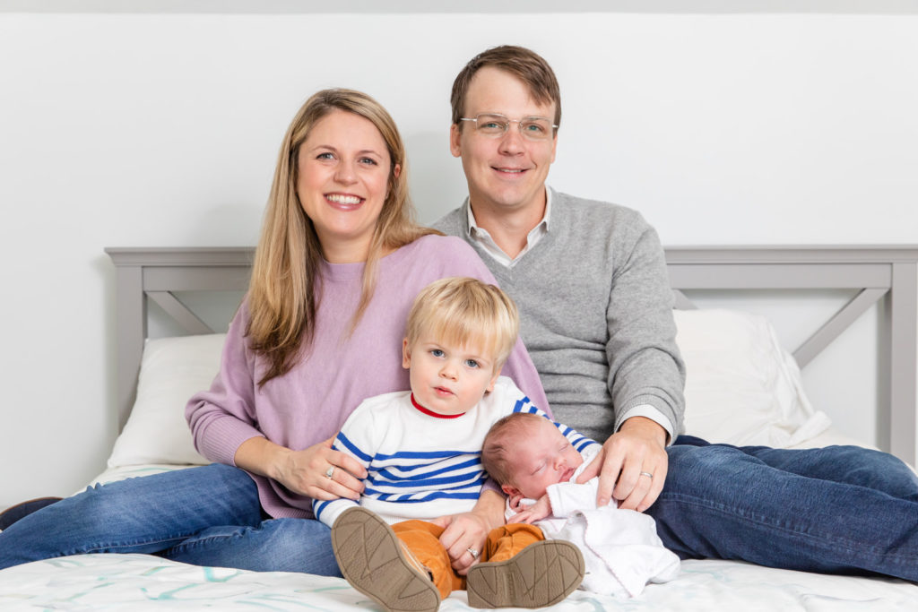 family with toddler and newborn sitting on parents bed during newborn session in Atlanta GA