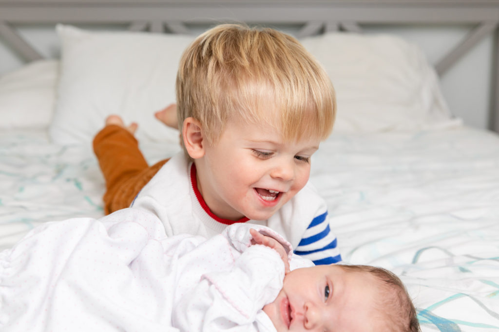 brother toddler laughing with newborn ion parents bed in Buckhead GA during newborn photo session