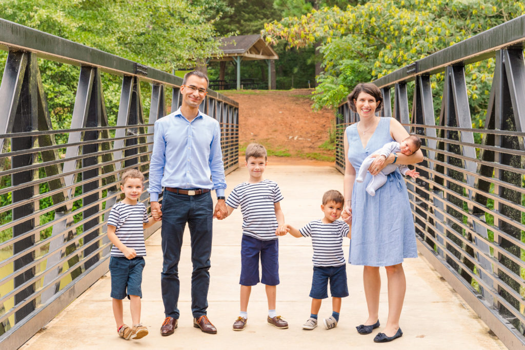 family with 4 little kids standing on a bridge holding hands during Brookhaven family photo session