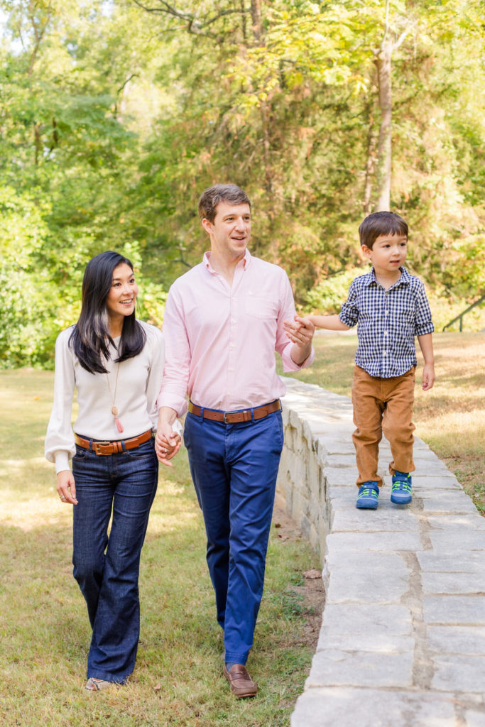 Parents and toddler walking and holding hands in a park during lifestyle photo session in Atlanta