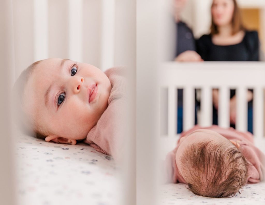 baby girl laying in crib and parents in the back blurry looking at her during milestone photo session