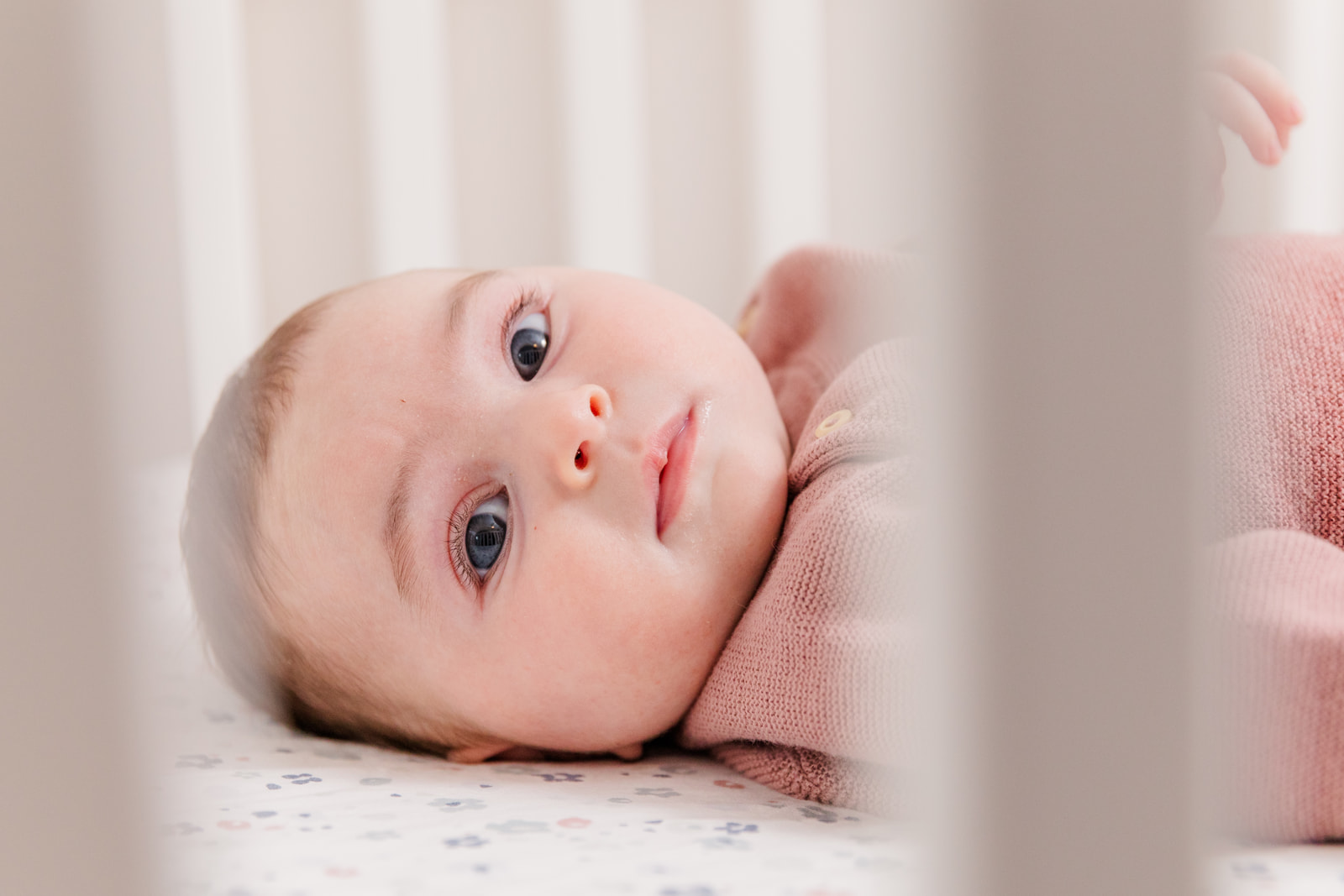 3 month old baby girl laying on crib and looking at camera