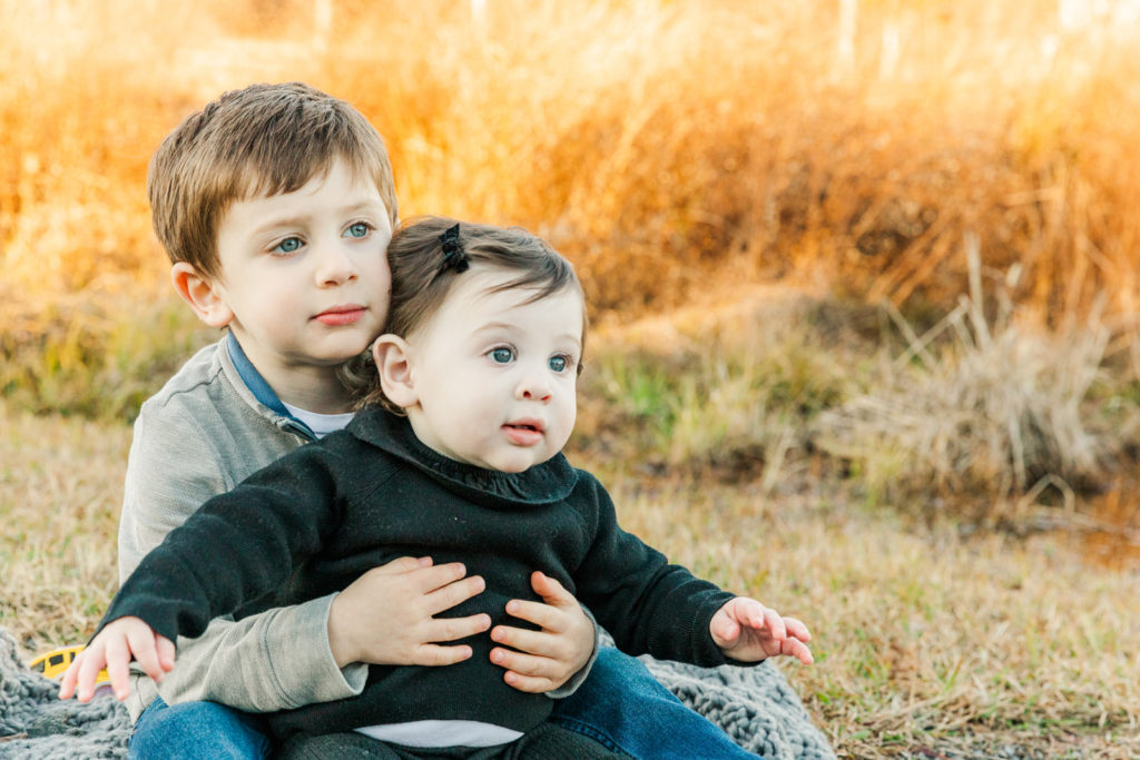 siblings toddler and baby sitting on a blanket in a park in Alpharetta during portrait session with atlanta photographer
