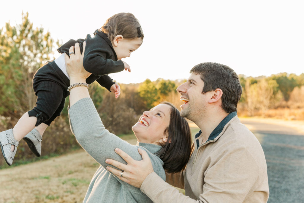 mom holding baby above her head and dad looking behind with GA family photographer