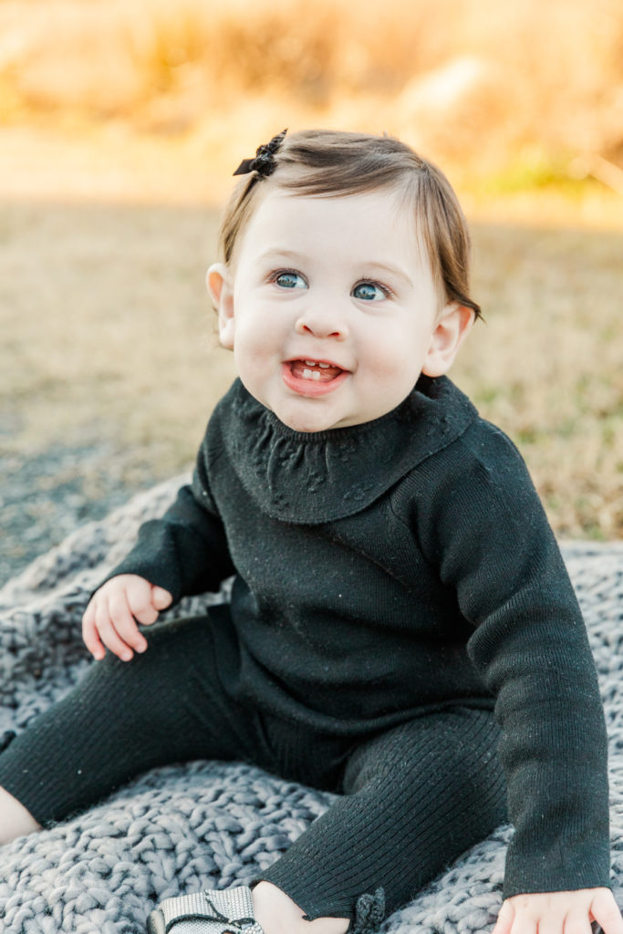 baby girl sitting on a grey blanket and smiling in a park with Atlanta photographer during milestone session