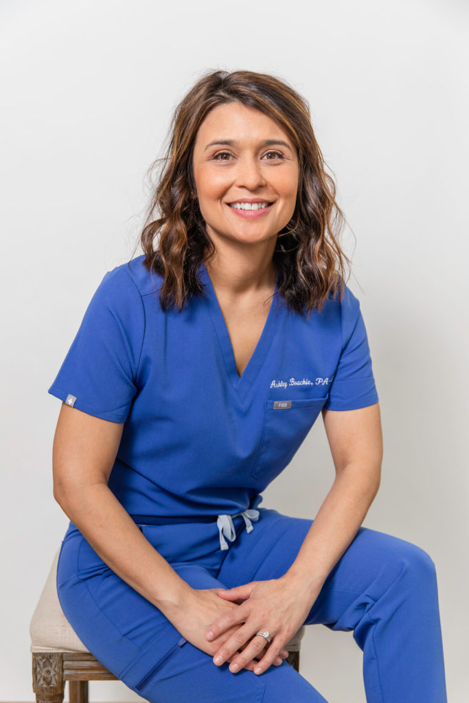 young doctor woman in blue scrubs outfit sitting in front of a white backdrop in studio Atlanta GA with Laure Photography during headshots session