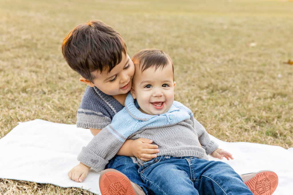 siblings boys toddler and baby hugging sitting on a blanket in a park with laure photography
