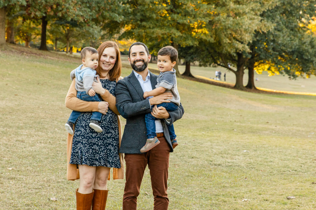 family picture parents holding toddler and baby standing on a park for fall photo session in blue and brown outfits