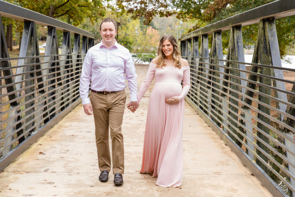 pregnant couple walking on a Brookhaven park bridge with light pink maternity dress by Laure Photography
