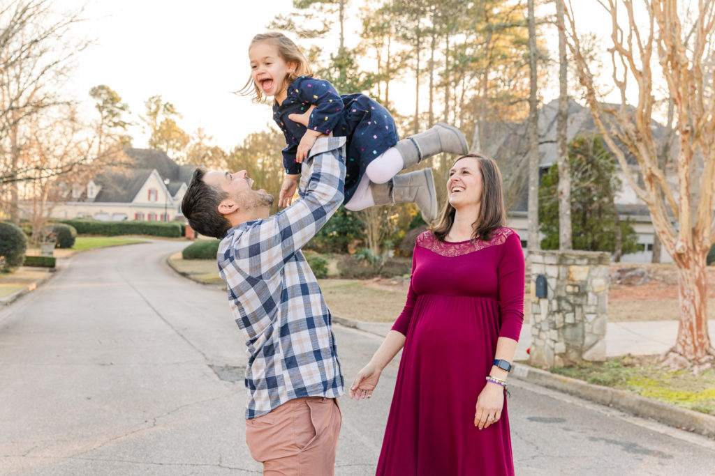 dad holding toddler girl high in the air during maternity session with pregnant mum on long pink dress with Atlanta photographer Laure Photography