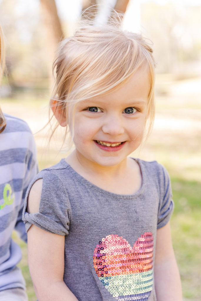 toddler girl in gray tee shirt smiling at the camera in a Buckhead park with Laure Photography Atlanta