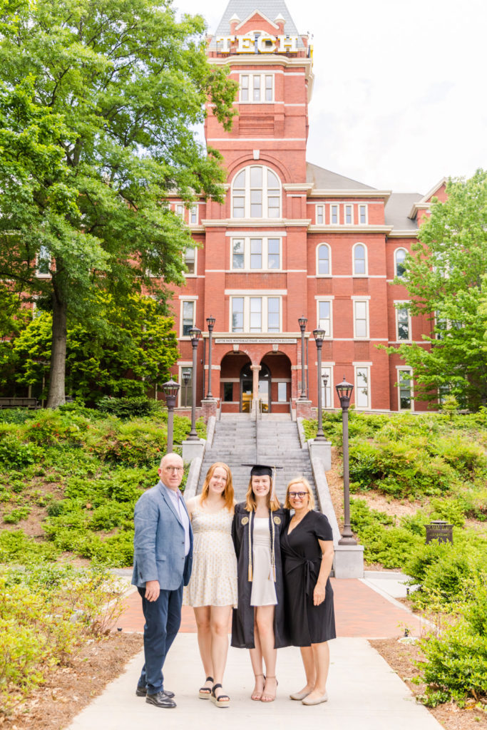 Graduate woman with her family with cap and grown standing in front of Georgia Tech Campus tower Atlanta by Laure Photography