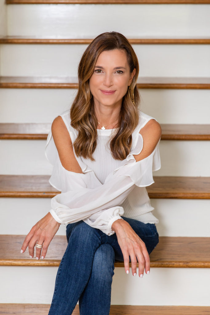 Interior designer wearing white top and jeans sitting on the stairs legs crossed and arms crossed looking at the camera during personal branding photo session by Atlanta brand photographer Laure Photography