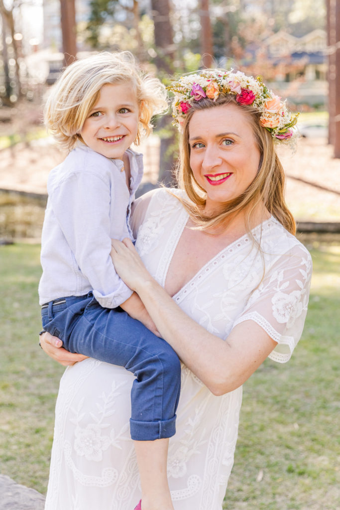 pregnant mom in long white lace dress and flower crown holding her son in her arms in Atlanta Duck Pond park with Laure Photography