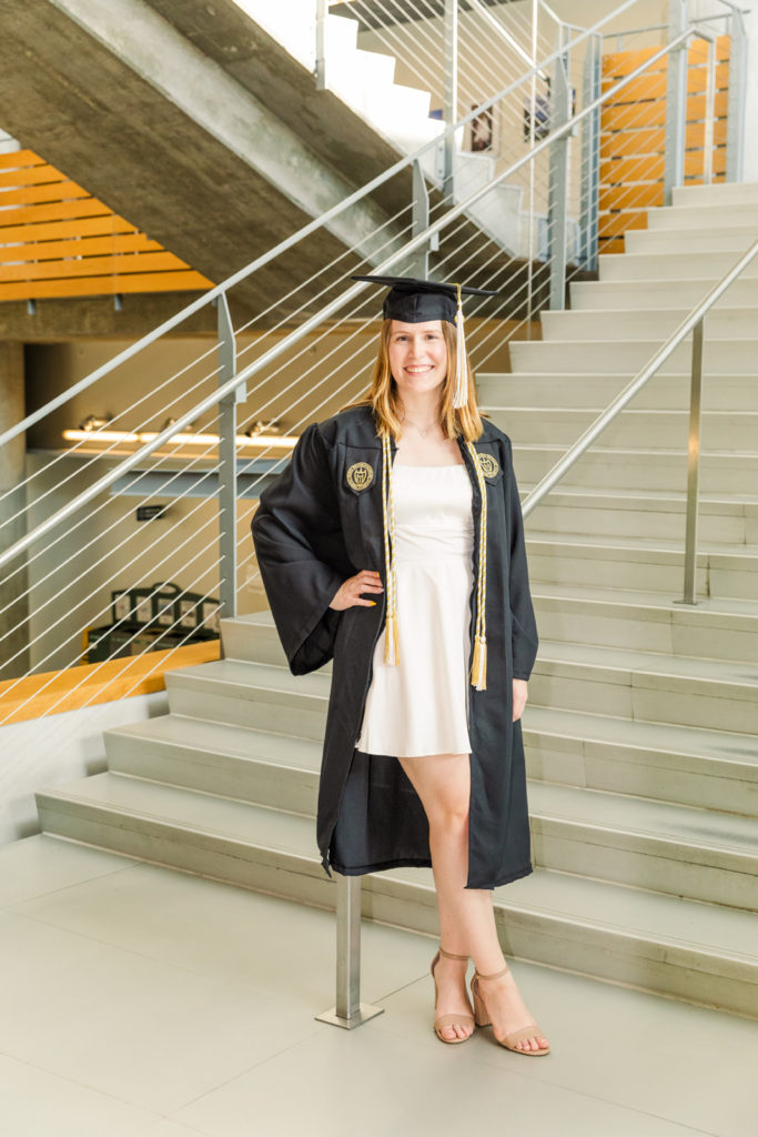 Graduate woman with cap and grown wearing white outfit in front of modern stairs on Georgia Tech Campus Atlanta by Laure Photography
