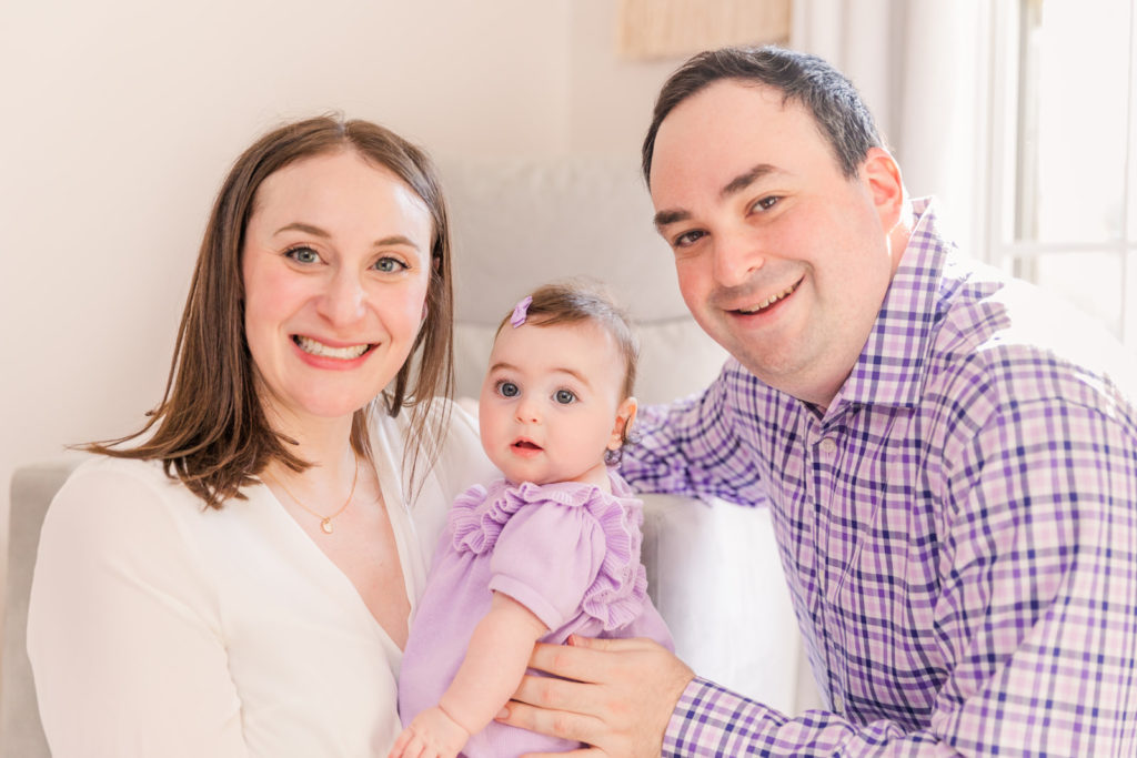 Parents with 6 month old baby girl in coordinated purple and white outfits in the nursery with Atlanta Laure Photography