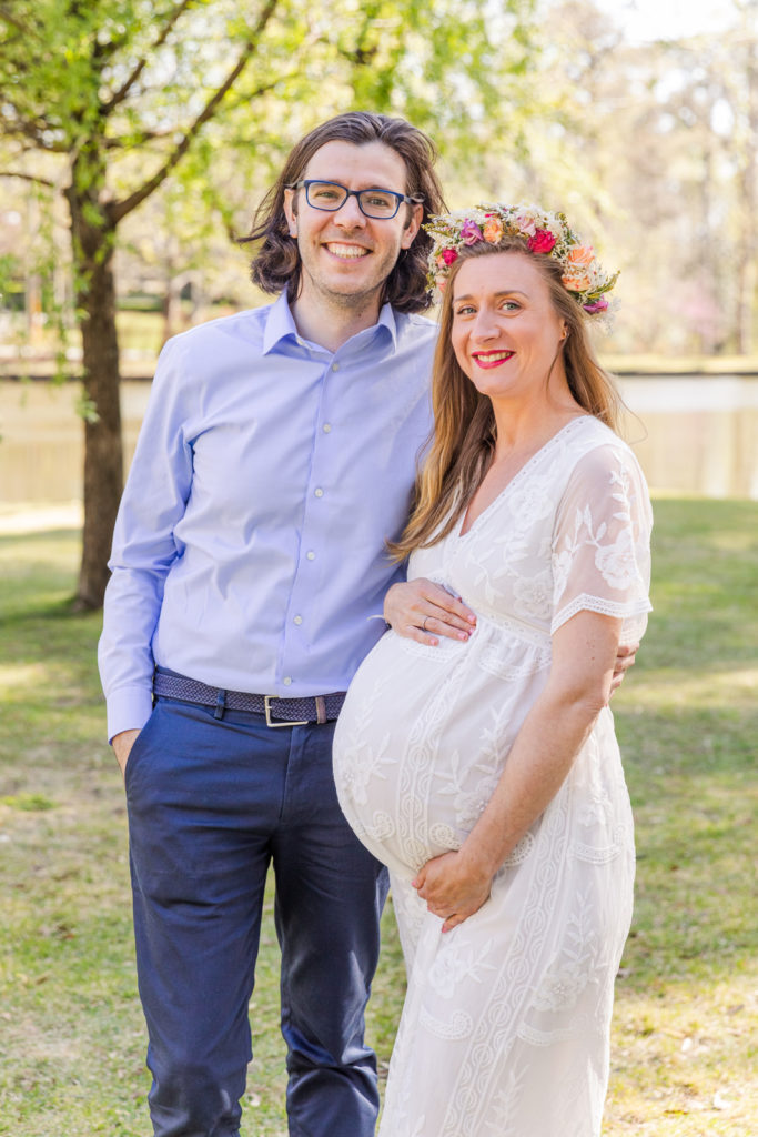 pregnant couple during their maternity session dad in coordinate blue outfit and mom in long white lace dress and flower crown in Atlanta Duck Pond park with Laure Photography