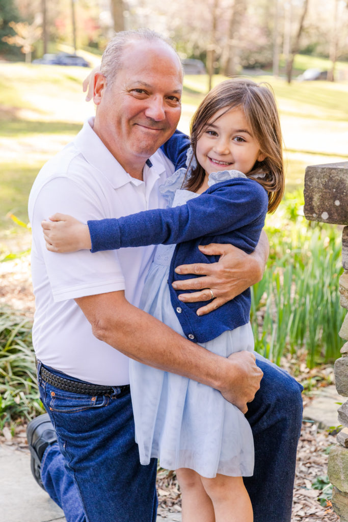 grandfather in jeans and white pool hugging grand daughter in light blue dress with Laure Photography Atlanta