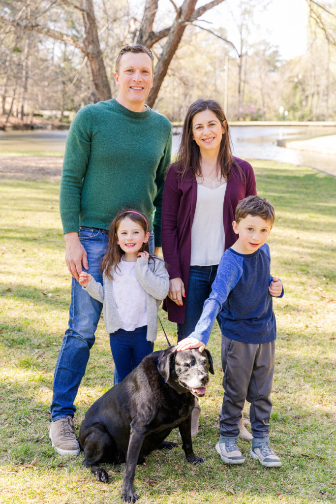family with dog standing wearing casual clothes in front of a pond with Laure Photography Atlanta