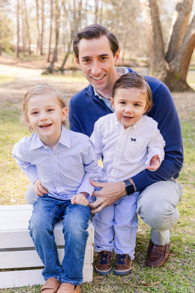 Date with toddler boys laughing at the camera and sitting on a white box near a pond wearing blue outfits with Laure Photography Atlanta