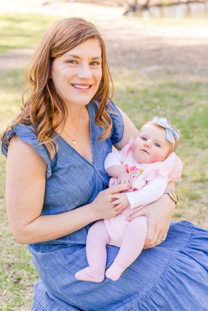 mom in blue jeans dress sitting and holding baby girl in pink outfit in a park with Laure Photography Atlanta