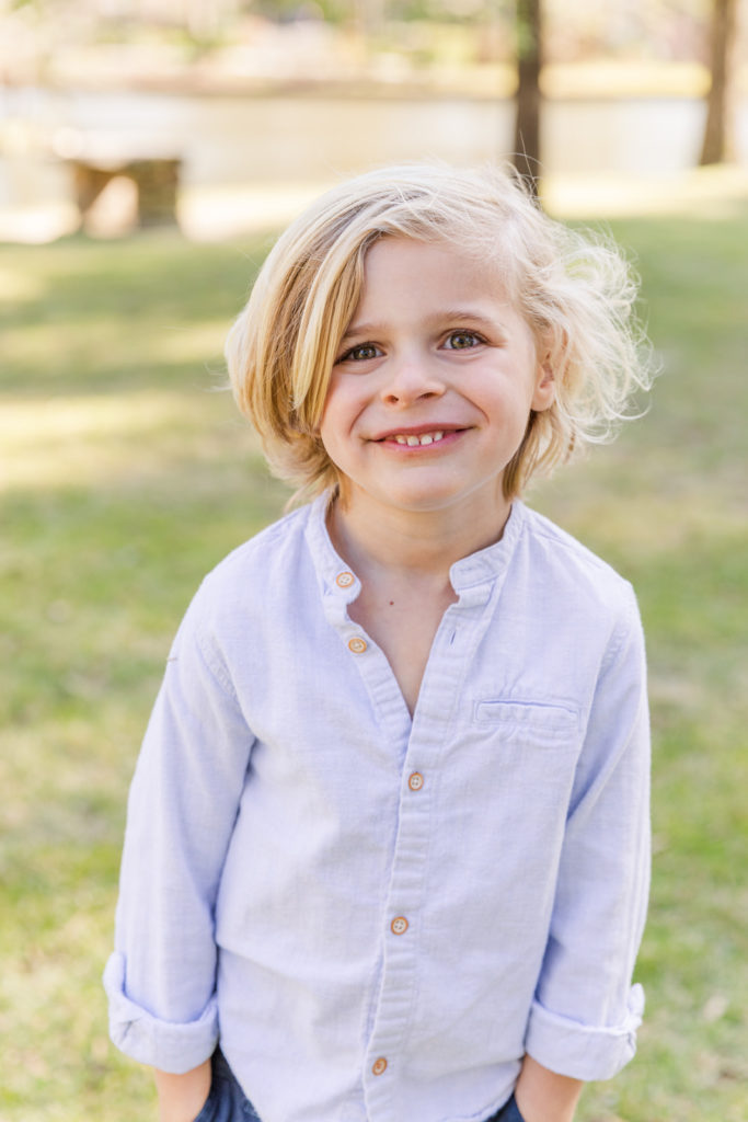 toddler wearing a clear blue shirt smiling with his hands in his pockets