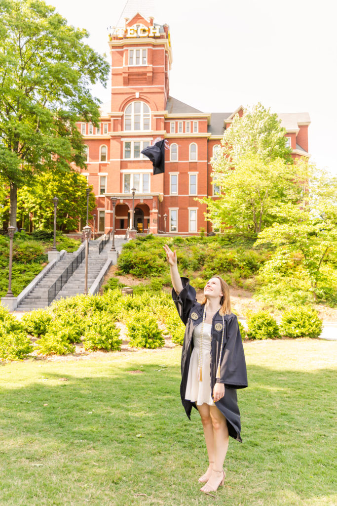 Graduate woman in grown throwing her cap in front of Georgia Tech Campus tower Atlanta by Laure Photography