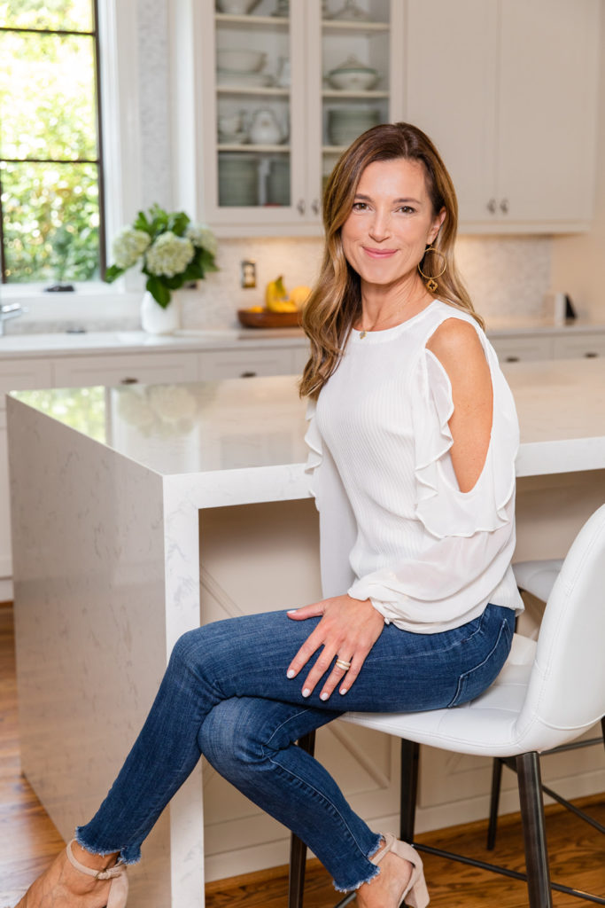 Interior designer wearing white top and jeans witting on the side of a bar stool chair legs crossed in a kitchen during personal branding photo session by Atlanta brand photographer Laure Photography