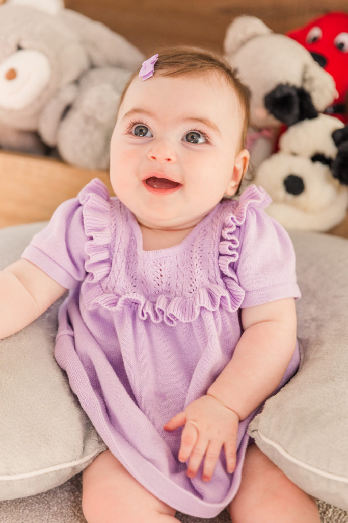 six month old baby girl sitting on the floor with her stuffed animals wearing a purple outfit and bow with Atlanta Laure Photography