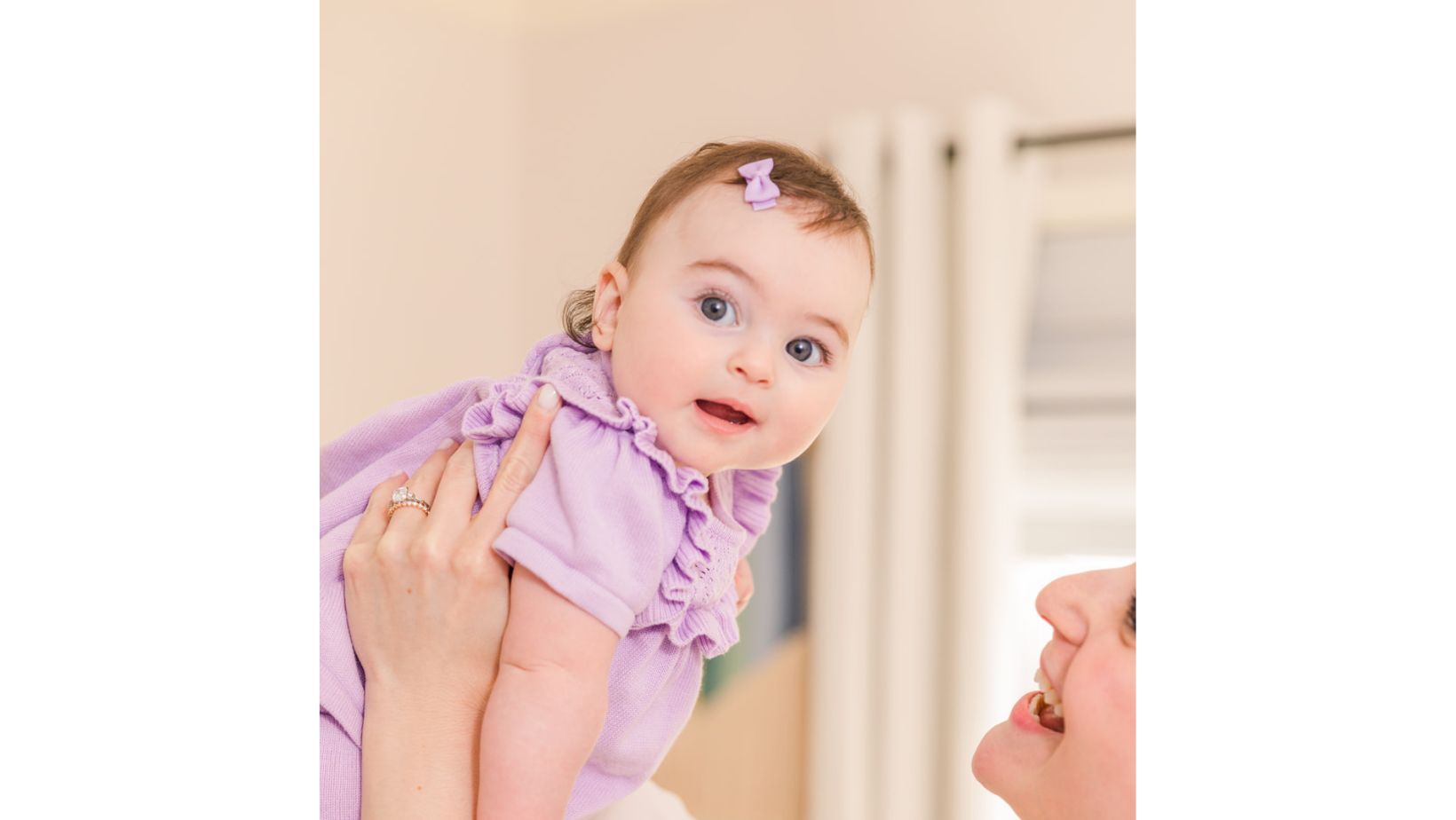 mom holding in the air baby six month old girl in purple outfit and purple bow