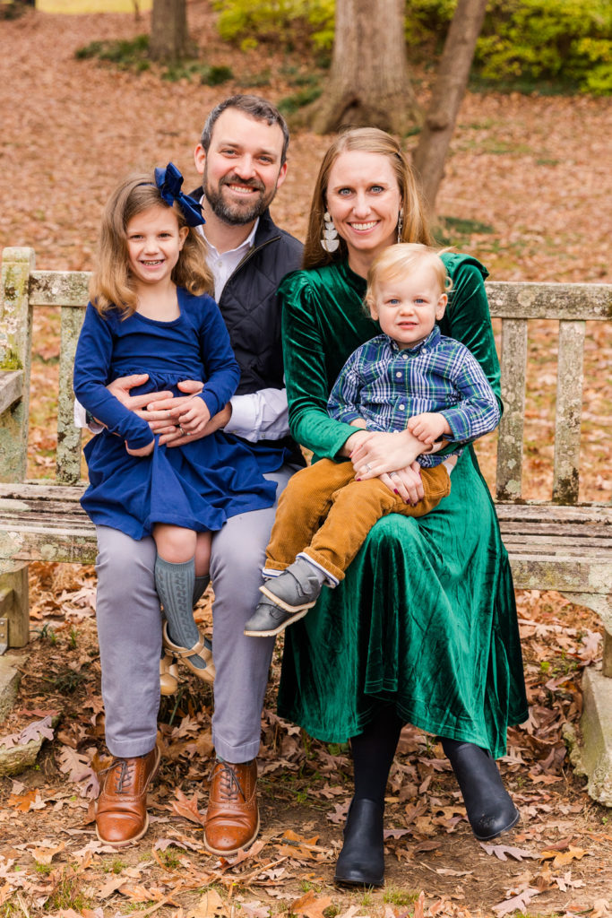 Family of 4 sitting on a wooden bench in an Atlanta park fall family photo session Laure Photography posed photo