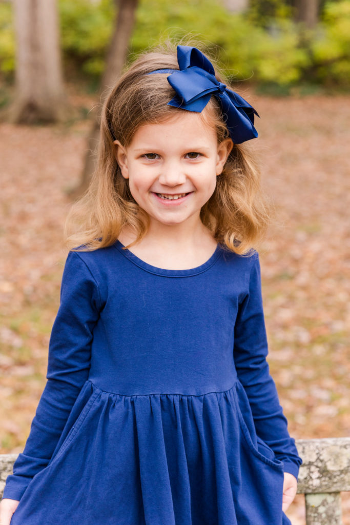 4 year old girl wearing blue dress and matching blue bow standing in an Atlanta park Laure photography