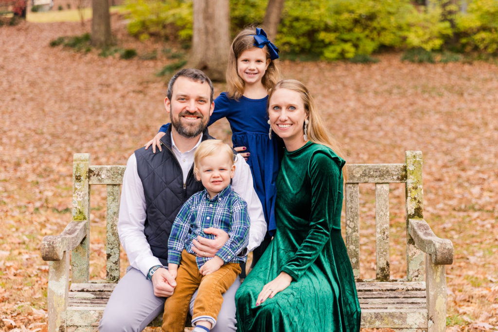 Family of 4 sitting on a wooden bench in an Atlanta Midtown GA park during family photo session Laure Photography posed photo