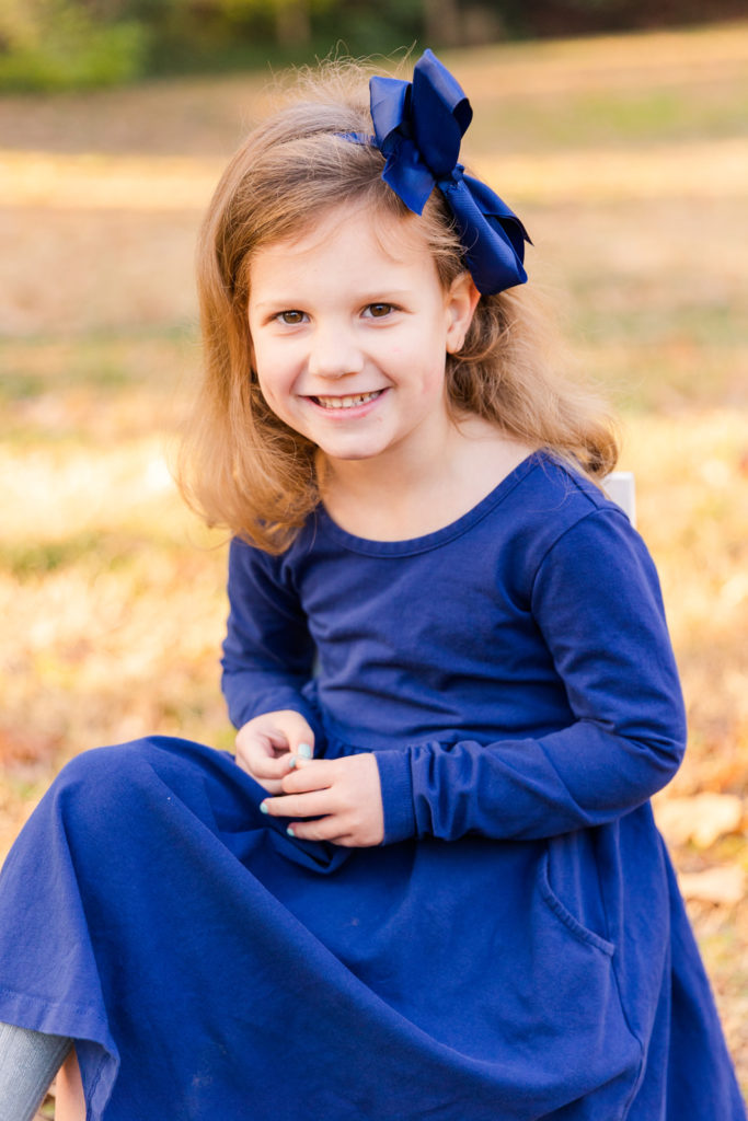 4 year old toddler wearing blue dress and matching blue bow sitting on a child chair posed in an Atlanta park Laure photography