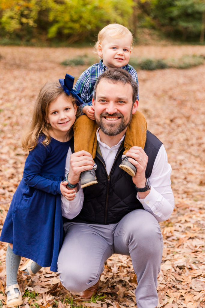 Dad kneeling down with a toddler boy in his shoulders and toddler girl hugging him in Atlanta GA park Laure photography lifestyle and posed family photo session