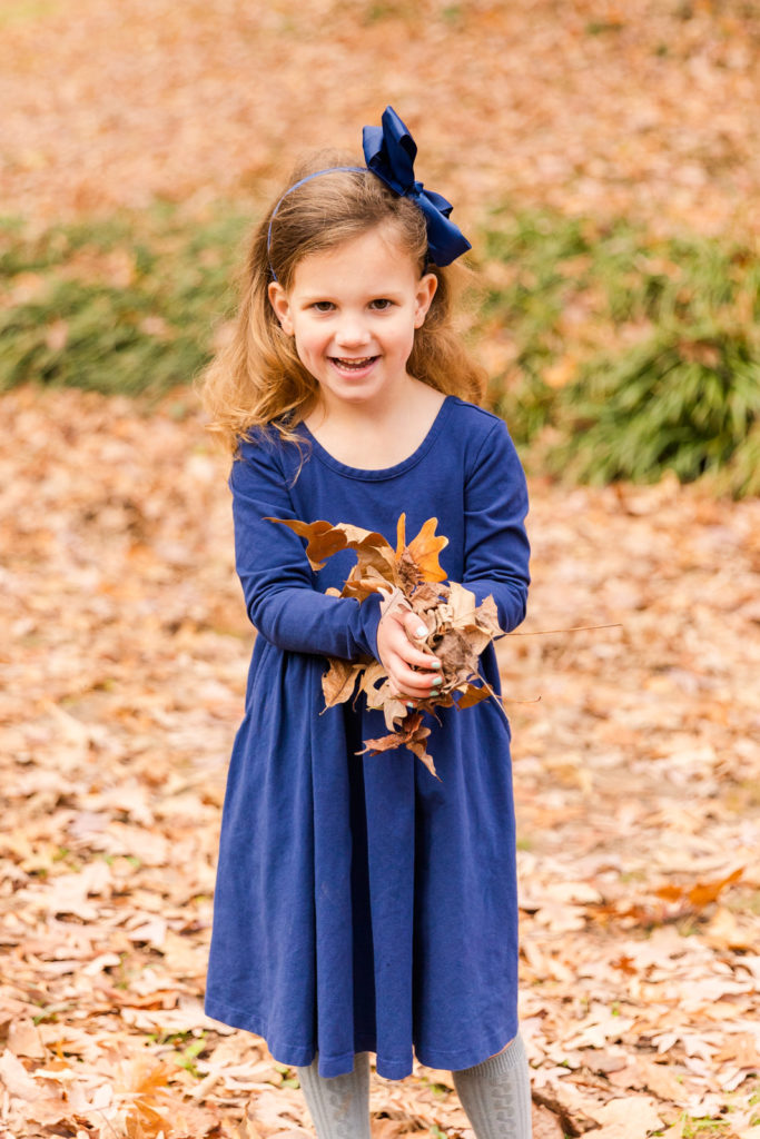 toddler girl wearing blue dress and matching blue bow throwing dead leaves in the air Atlanta GA park Laure photography lifestyle family photo session