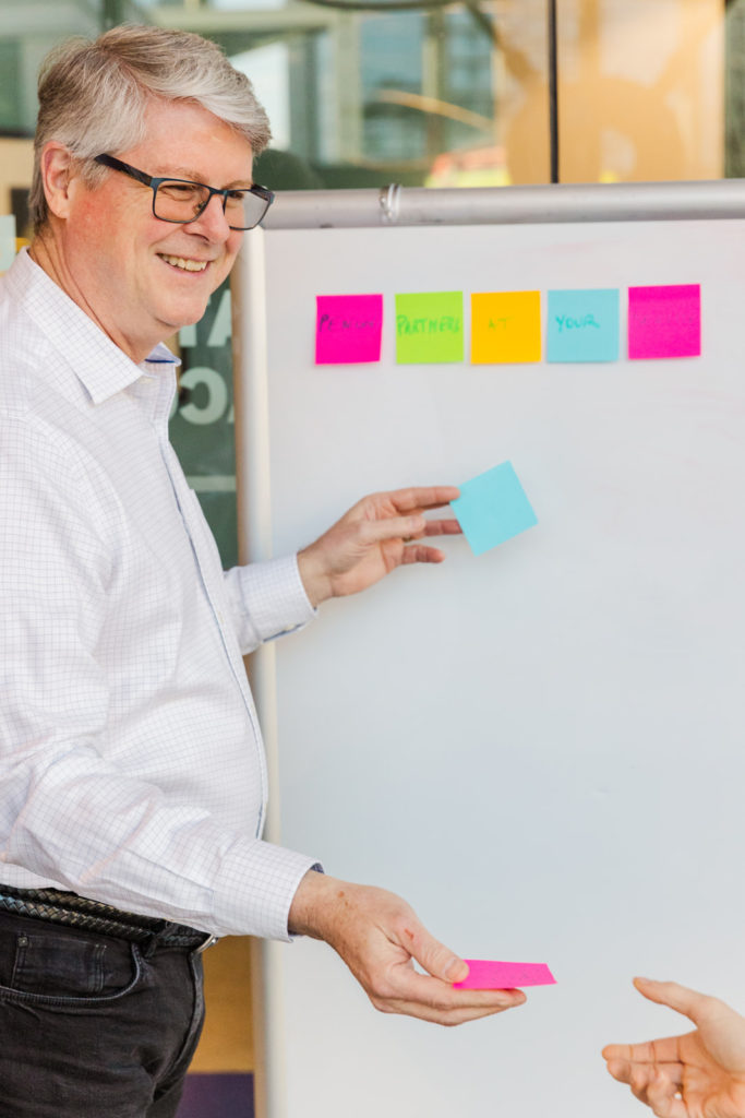 man standing in front of a white board working with post its during a team meeting in a conference room Laure Photography