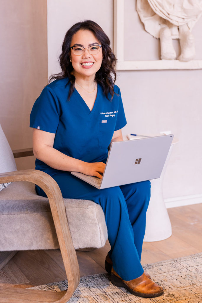 surgeon doctor wearing in blue scrubs witting on an armchair working on her computer during brand photo shoot Laure Photography