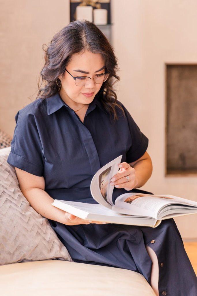 woman wearing long buttoned up black dress sitting on a sofa and reading a book during her brand photo shoot with Atlanta photographer Laure Photography branding