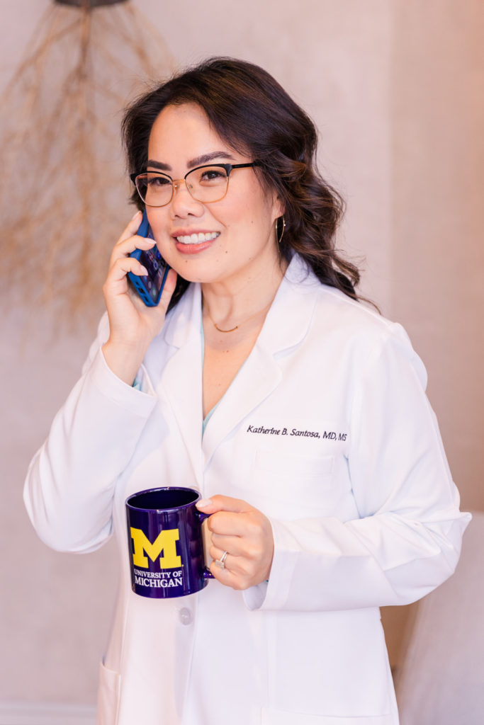 Woman doctor in white coat standing and taking on the phone while holding a Michigan coffee mug Laure Photography brand session