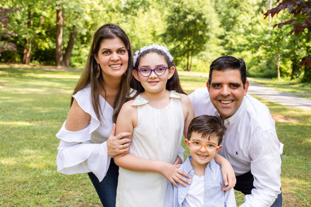 family picture or parents and two children mom and dad wearing white top and blue jeans daughter wearing a white dress and white flower headband in a Sandy Spring park GA with Laure Photography