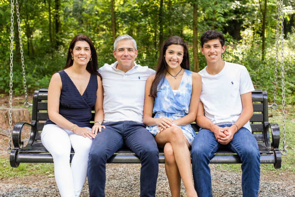 parents with teenager siblings sitting on a swing all wearing blue and white outfits with GA photographer Laure Photography