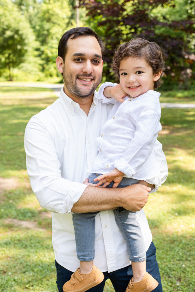 Dad holding toddler in his arms, both wearing white shirt and blue pant in a park Atlanta family photographer Laure Photography
