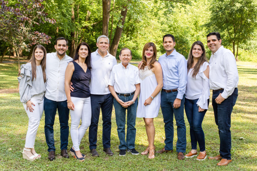 Two generations of nine adults dad and siblings standing in an Atlanta GA park wearing coordinated white and blue outfits with family photographer Laure Photography