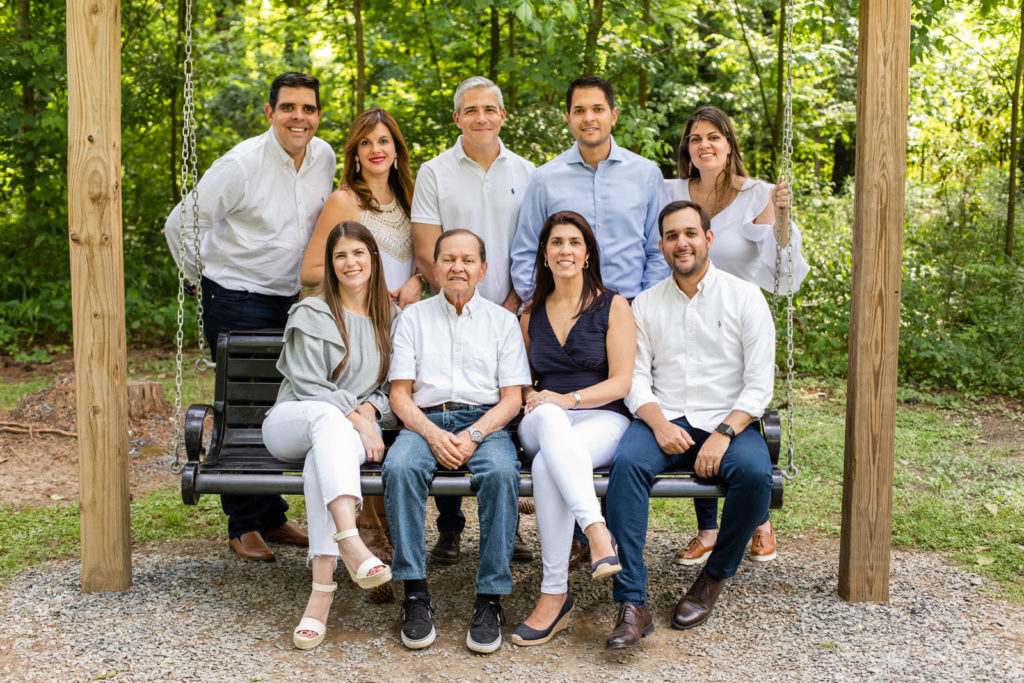 Two generations of nine adults sitting on a swing in a park wearing coordinated white and blue outfits with family photographer Laure Photography