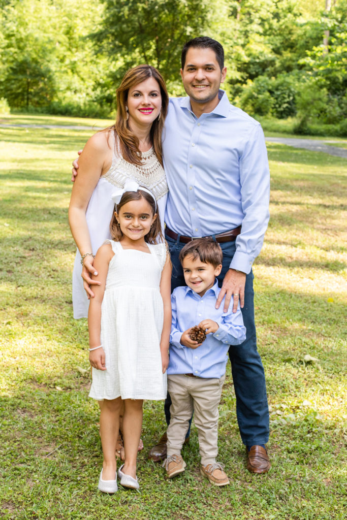 Family of 4 parents standing with toddlers in front of them wearing coordinated white and blue outfits during multi-generation family photo session with Laure Photography in Atlanta GA