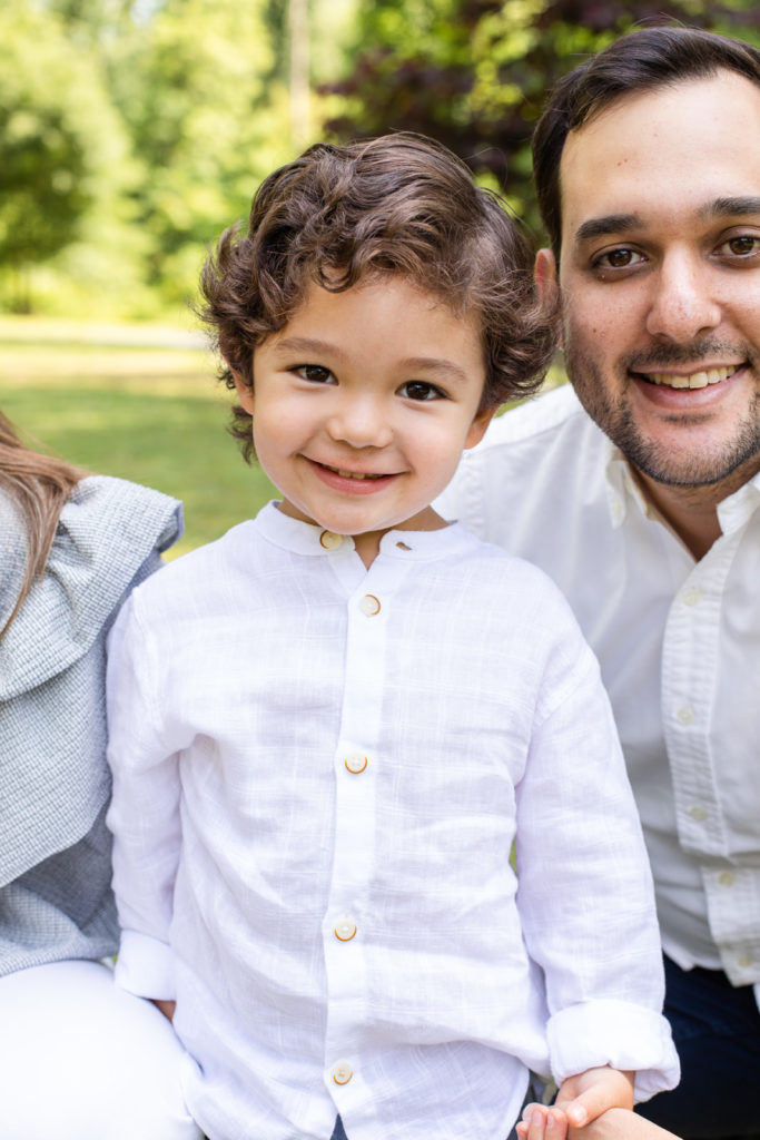 toddler boy wearing a white linen top smiling during a family photo shoot in a park with Laure Photography